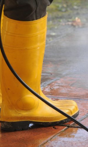 persona-vestida-botas-goma-amarilla-boquilla-agua-alta-presion-limpiando-suciedad-baldosas